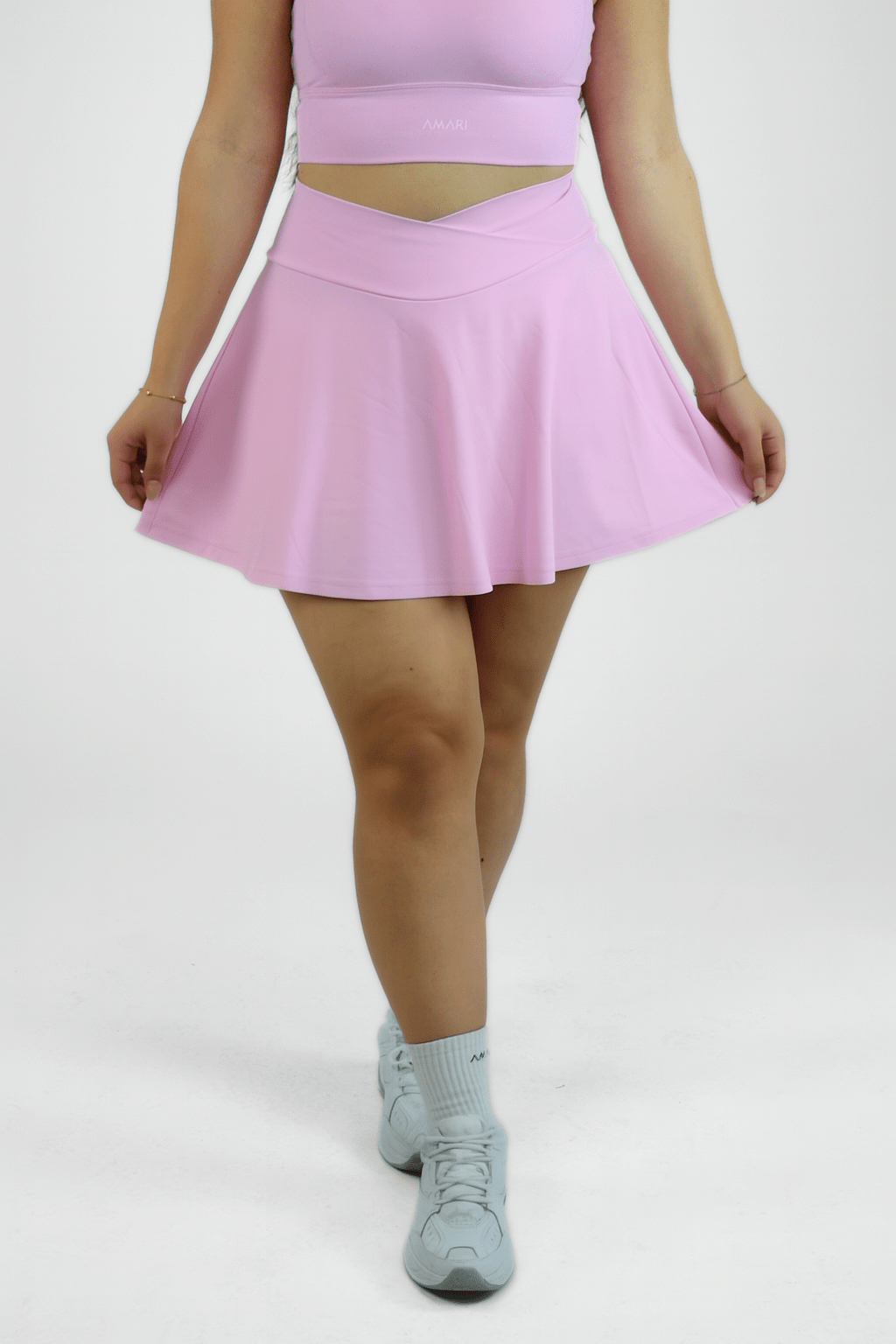 Person wearing a pink skirt and light blue sneakers on a white background